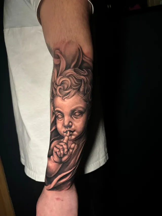 Sculptural realism forearm tattoo of a cherub holding a finger to its lips